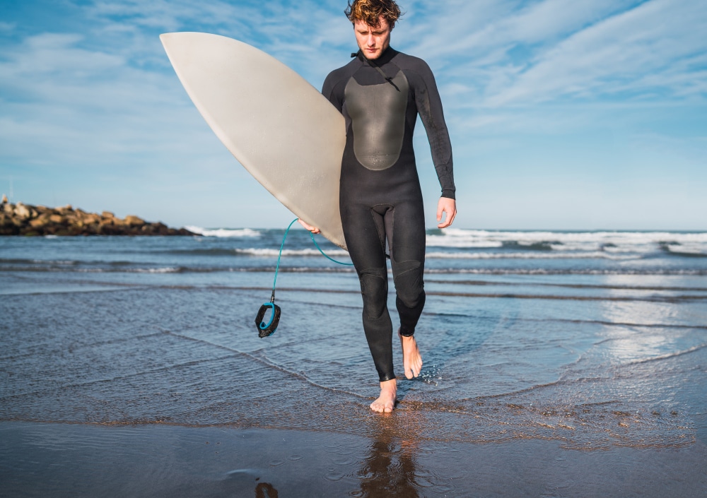 Image of a man wearing neoprene wetsuit and holding a surfboard